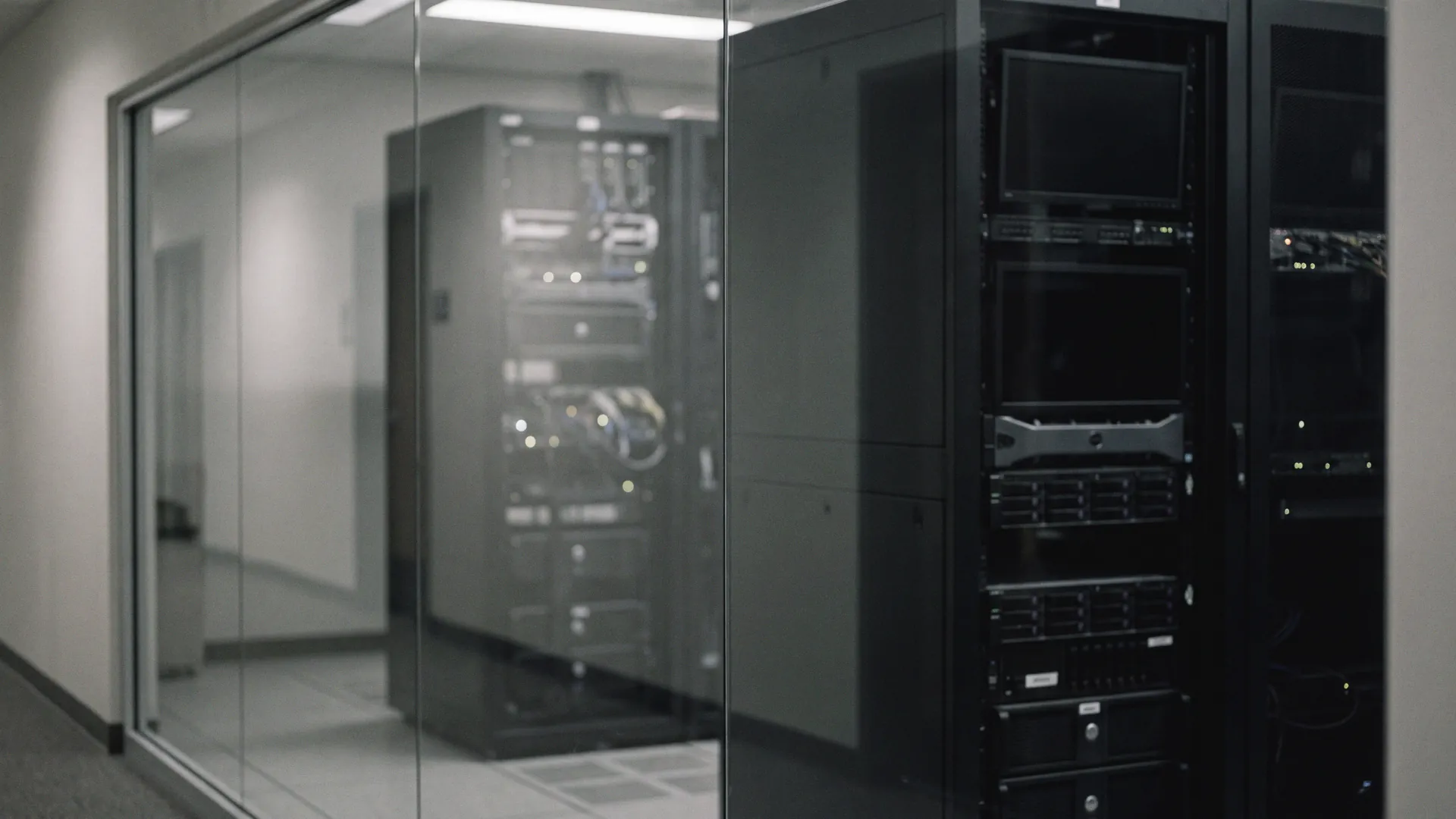 Racks of network equipment and cabling seen through a glass wall in cool light, heavily defocused.